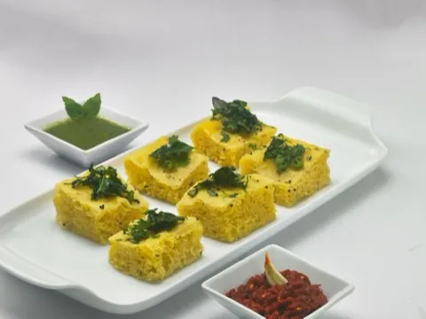 Dhokla squares topped with tempering, served with green and red chutney.