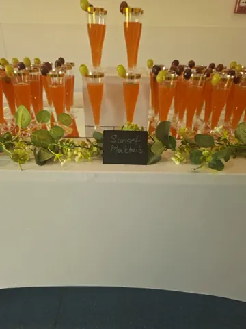 Rows of sunset mocktails in gold-rimmed flutes behind a chalkboard sign.